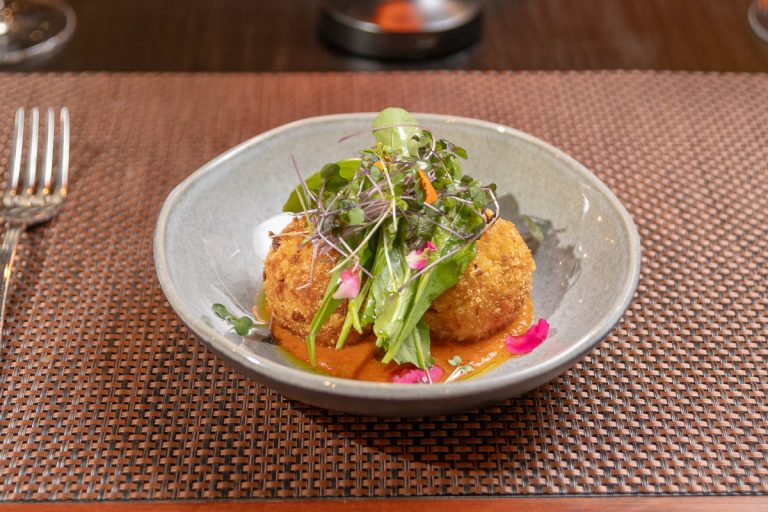 Arancinis Rellenos: Croquetas de arroz carnaroli al estilo italiano, rellenas de mozzarella y tomate, servidas sobre salsa romesco y mix de hojas.
