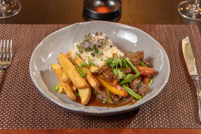 Lomo Saltado: Tradicional salteado de lomo vacuno al estilo peruano, con vegetales, acompañado de papas fritas y arroz blanco.